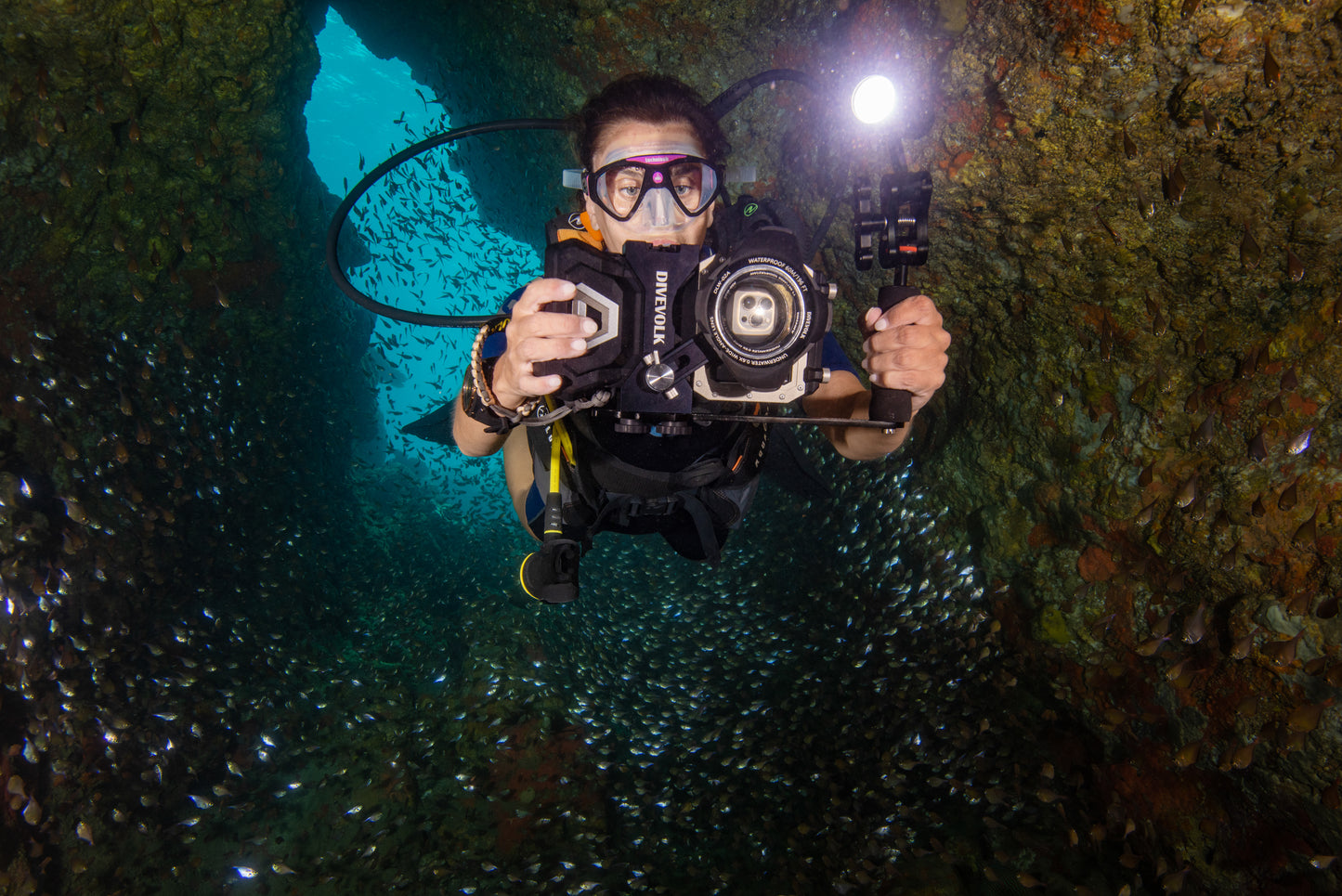 A SCUBA Diver swims through an underwater cave using their phone to take photos and videos underwater in the Divevolk Seatouch 4 Max Waterproof phone housing Creator Kit