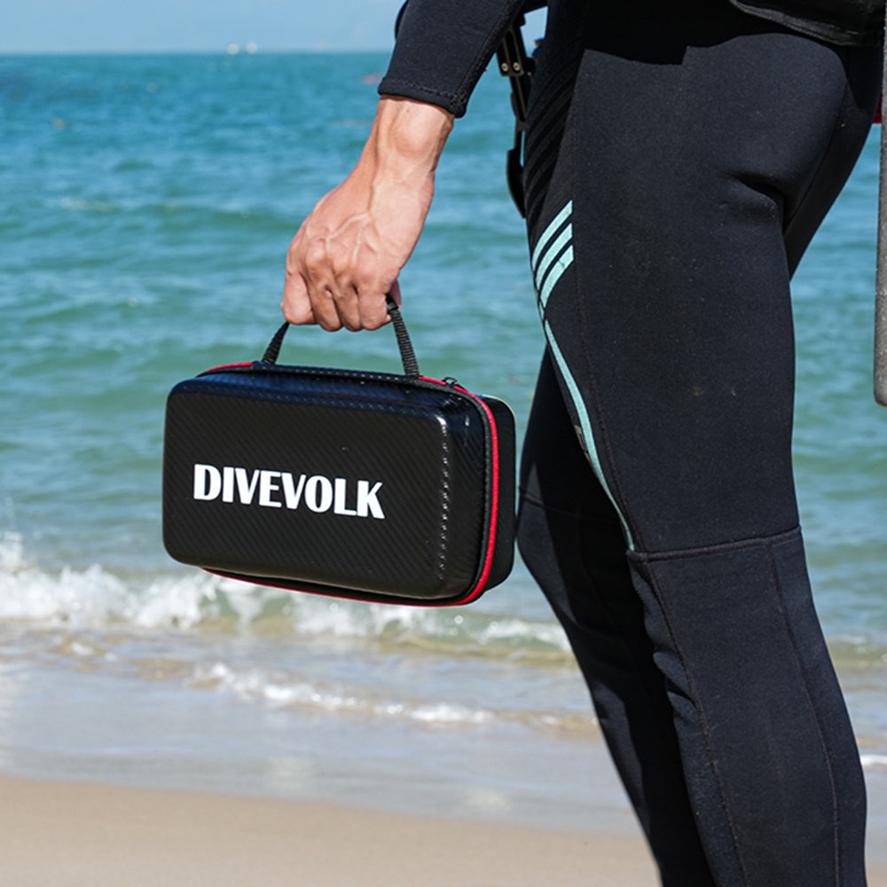 Person in wetsuit holding a Divevolk case on a beach