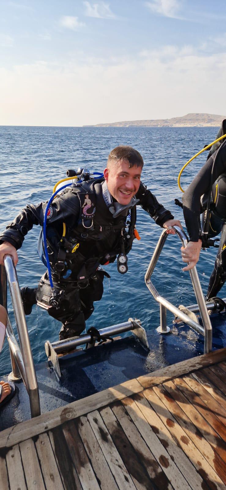 Person in scuba diving gear stepping onto a boat with water and sky in the background