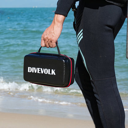 Person in wetsuit holding a Divevolk case on a beach