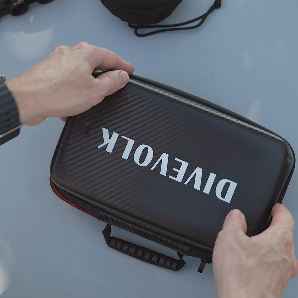 Person holding a black case with 'Divevolk' branding on a light blue surface