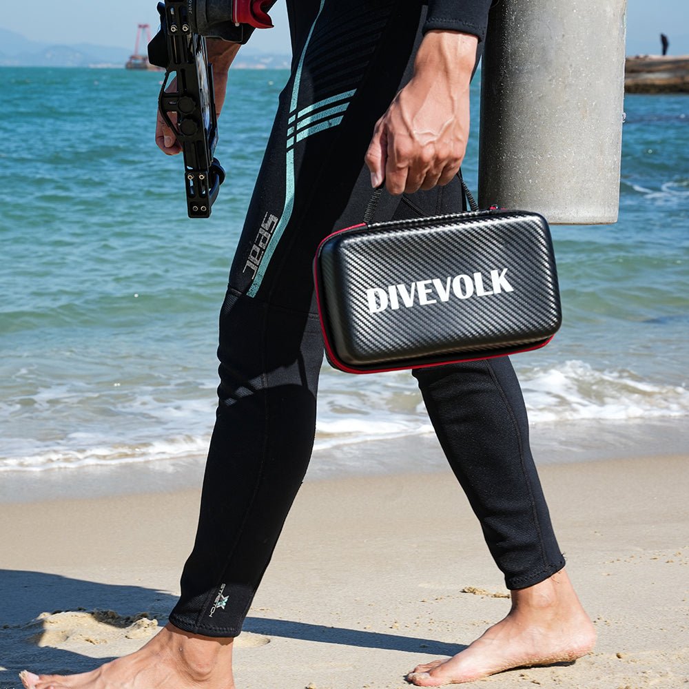 Scuba Diver holding a Divevolk case on a beach with ocean in the background