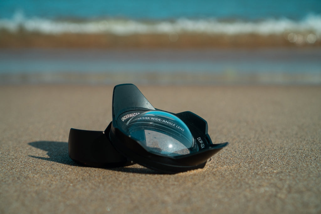 The Divevolk DLW - 02A Wide - Angle Conversion Lens lies on the sand of a beach