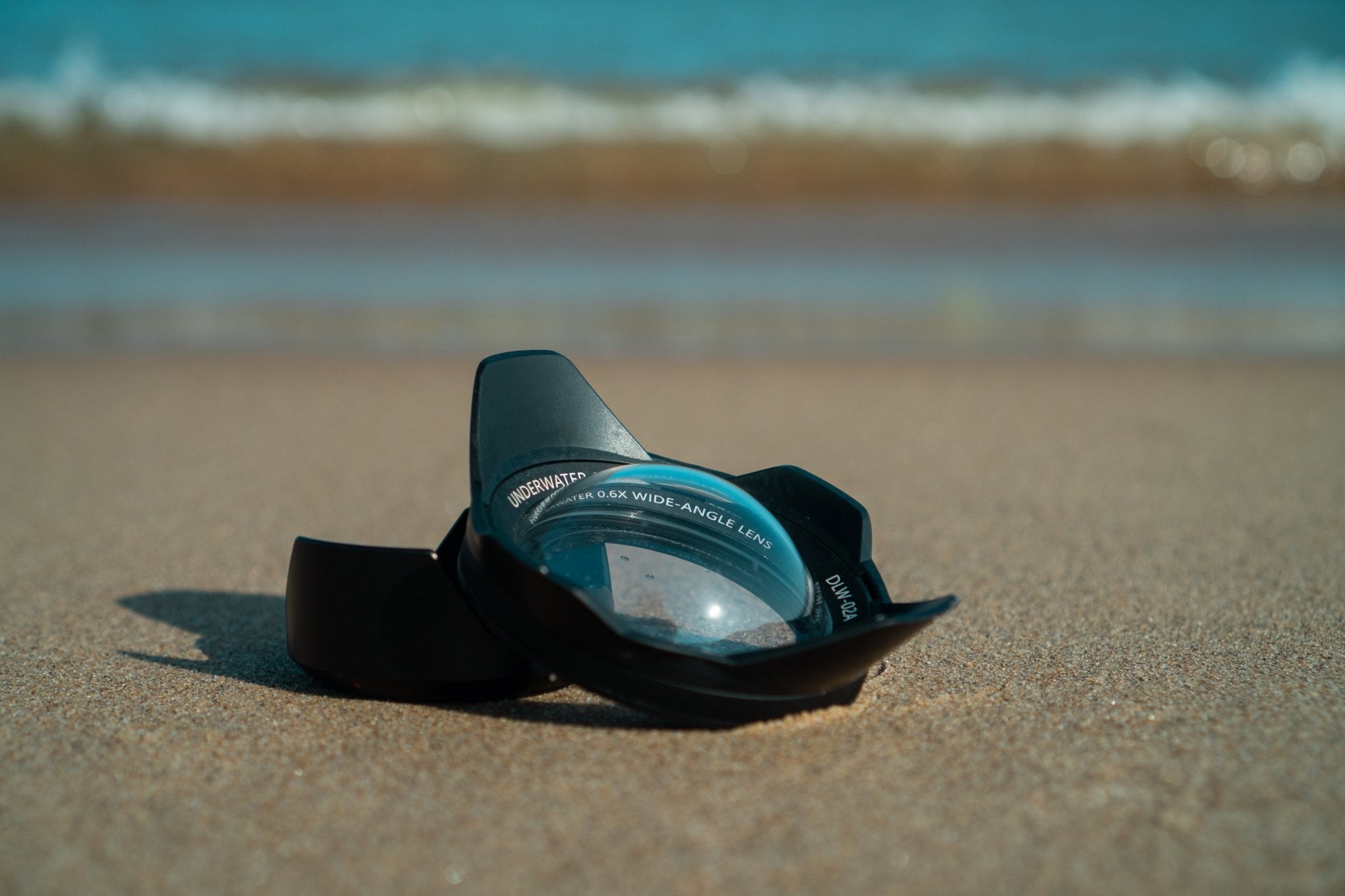 The Divevolk DLW - 02A Wide - Angle Conversion Lens lies on the sand of a beach